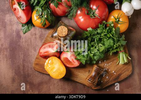Frische Tomaten Paprika Kräuter Knoblauch auf hölzernem Schneidebrett mit Salz Pfeffermühle angeordnet. Bunte Gemüse-Kochzutaten Stockfoto