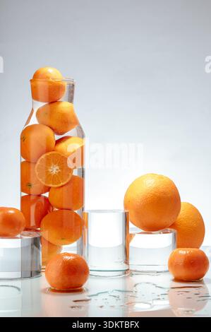 Orangen und Mandarinen in einem Glasgefäß und auf einem Tisch. Stockfoto