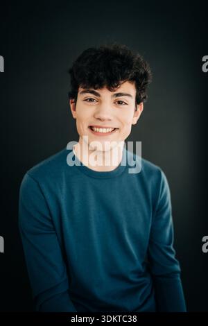 Lächelnder junger Mann in blauem Hemd vor dunklem Studiohintergrund Stockfoto