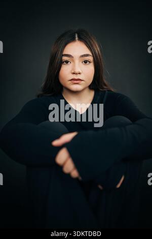 Eine junge Frau sitzt und blickt aufmerksam in die Kamera Stockfoto