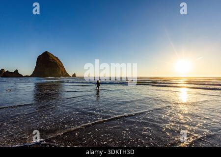 USA, Oregon, Cannon Beach, eine Frau, die bei Sonnenuntergang in der Nähe von Heuhaufen-Felsen weht Stockfoto
