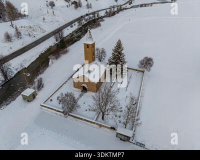 Aus der Vogelperspektive auf eine schneebedeckte Kirche mit einem hohen Turm, die inmitten einer ruhigen, frostigen Landschaft steht und die kalte Luft beißt, Sils im Engadin/Segl, Grigi Stockfoto
