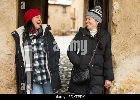 Zwei lächelnde Frauen in Wintermänteln und Hüten stehen in einem alten Eingang Stockfoto