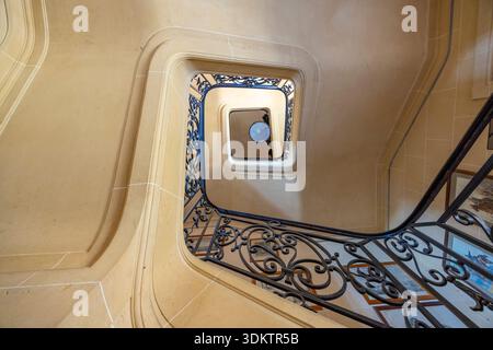 Blick hinunter auf eine wunderschöne Wendeltreppe aus Stein mit einem kunstvollen dunklen Metallgeländer Stockfoto