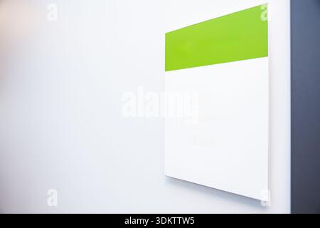Ein modernes Schild zur Wandmontage mit weißem Sockel und grünem Oberteil, das an einer weißen Wand mit dunkler vertikaler Kante auf der rechten Seite steht. Stockfoto