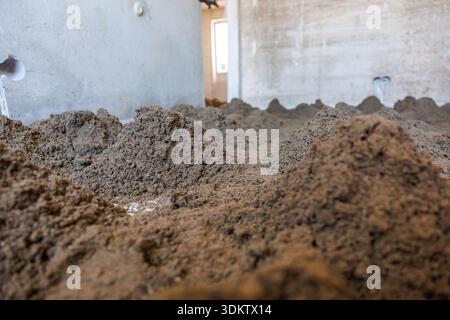 Baustelle im Innenbereich mit losen Bodenpfählen auf dem Boden, unlackierten Betonwänden, sichtbaren Steckdosen und Licht, das durch eine Tür eindringt Stockfoto