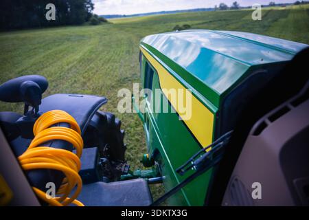 Nahaufnahme von Landmaschinen mit Zugmaschinen. Gelber Spiralschlauch, schwarzer Kotflügel und reflektierende Kapuze zeigen moderne Ausrüstung in der Mittagszeit Stockfoto
