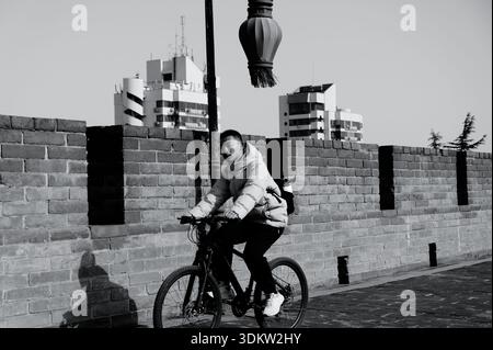 Radfahrer fahren entlang der Xi'an Stadtmauer in Schwarz und weiß, vorbei an Backsteinmauern mit modernen Gebäuden, die dahinter ragen Stockfoto