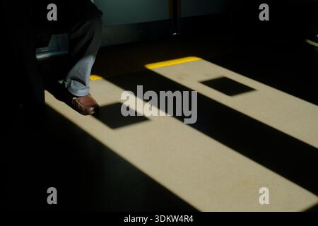 Dramatisches Licht und Schatten auf dem Bahnboden mit dem Bein des Fahrgastes in einem japanischen Pendlerzug Stockfoto