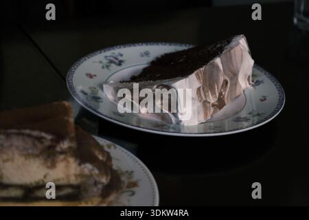 Nahaufnahme mit köstlichem Tiramisu-Kuchen, serviert auf einem Teller mit Blumenmuster in einem stimmungsvollen Café in Yokohama, Japan Stockfoto