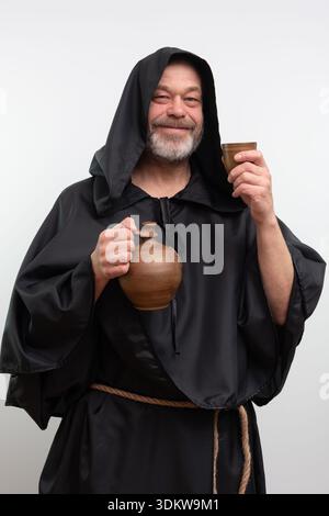 Männlicher Mönch lächelt und hält Tonbecher und Krug. Stockfoto