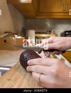 Reife Avocado mit Messer auf Holzbrett in der Küche schneiden Stockfoto