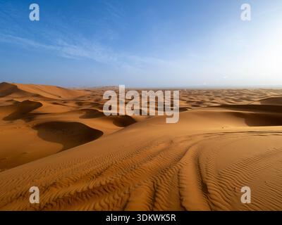 Weitläufige Luftaufnahme der endlos welligen goldenen Sanddünen, die sich bis zum fernen Horizont unter einem hellblauen Himmel in der Erg Chebbi Region von Mor erstrecken Stockfoto