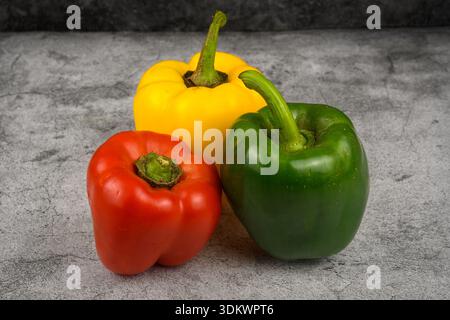 Drei frische Paprika in Rot, Grün und Gelb auf grauem Betonhintergrund. Minimales gesundes Essen Stillleben mit Kopierraum, Frühlingsfarben. Stockfoto