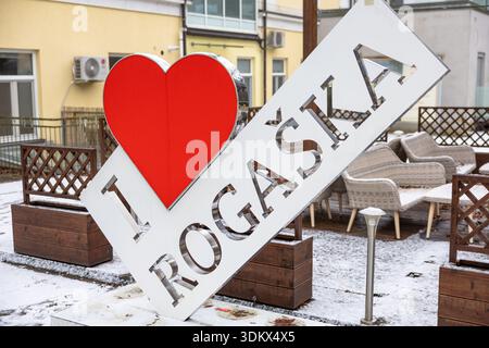 Winterszene im Freien mit einem großen weißen Schild mit einem roten Herzen und den Worten I Love Rogach, umgeben von Korbsitzen, hölzernen Pflanzgefäßen und a s Stockfoto