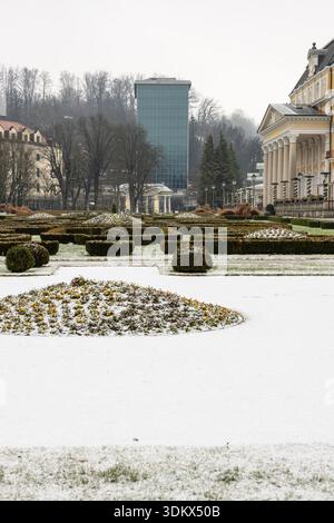 Eine ruhige Winterszene mit einem formellen Garten mit getrimmten Hecken, schneebedeckten Blumenbeeten, einem großen gelben neoklassizistischen Gebäude und einem eleganten Glasdach Stockfoto