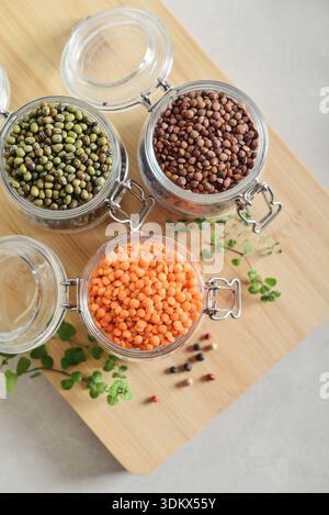 Rohe rote und braune Linsen mit trockenen Mungbohnen in einem Glas mit Gewürzen und Kräutern auf hölzernem Schneidebrett Nahaufnahme. Vielfalt an gesunden veganen, Pflanzen b Stockfoto