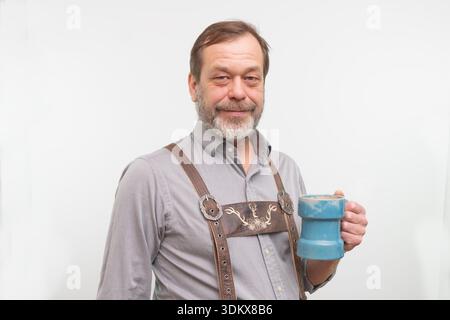 Bärtiger Mann in bayerischer Tracht posiert mit Keramikbecher im Studio Stockfoto