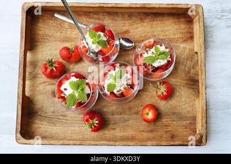Frische Erdbeerparfaits mit Schlagsahne und Minze auf einem Holztablett. Draufsicht Stockfoto