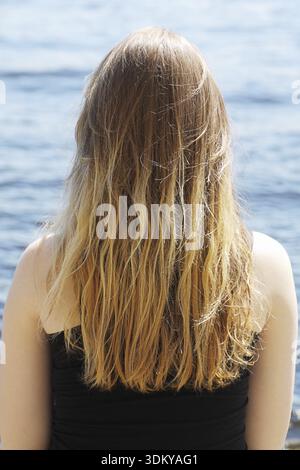 Mädchen mit blonden langen Haaren sitzen am Wasser zurück zum Betrachter Stockfoto
