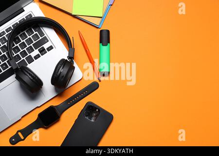 Kopfhörer, Laptop, Smartphone, Smart Watch und Schreibwaren auf orangefarbenem Hintergrund, flach gelegt. Leerzeichen für Text Stockfoto