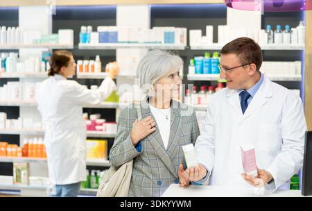 Pharmazeutischer Mann mittleren Alters, der alte Kundschaft über Pflegemittel in Box berät Stockfoto