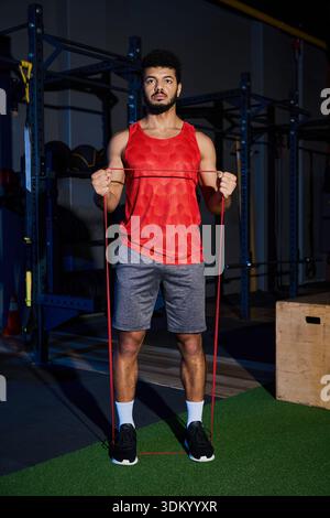 Der energiegeladene junge Mann mit Bart konzentriert sich auf sein Workout mit Widerstandsbändern in einem Fitnessstudio. Stockfoto
