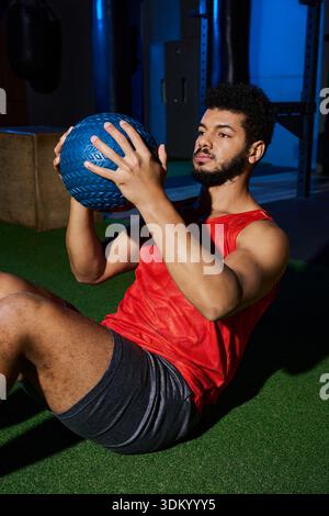 Ein junger Afroamerikaner mit Bart arbeitet intensiv in einem Fitnessstudio mit einem gewichteten Ball. Stockfoto