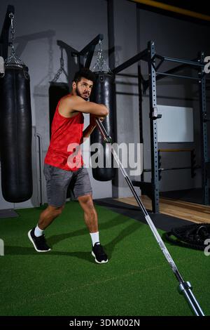 Ein selbstbewusster junger Mann mit Bart konzentriert sich auf sein Workout mit Gewichten in einer lebendigen Fitnessumgebung. Stockfoto