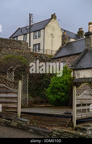 Die historische Architektur von Portsoys Altstadt zeigt Steinbauten und Schieferdächer. Ein Holzzaun und ein grüner Gartenbereich stehen im Vordergrund auf einem V Stockfoto