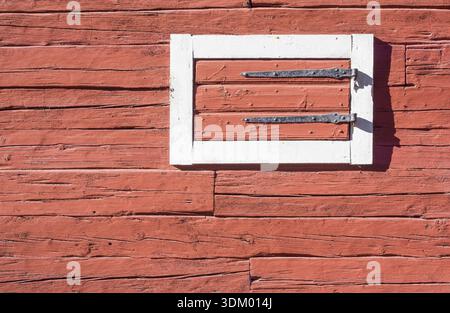 Rote Blockhauswand mit Schraffur. Detail eines traditionellen schwedischen, rot lackierten Blockhauses mit weiß lackierten Zierleisten um die Luke. Stockholm, Schweden Stockfoto