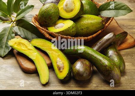 Frische, reife Avocados auf einem rustikalen Holztisch mit ganzen und geschnittenen Früchten mit lebendigem grünem Fleisch und natürlichen Texturen. Stockfoto