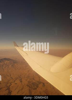 Dramatische Luftaufnahme von einem Passagierfenster um 07:55 UHR am 11. September 2018, kurz nach dem Start vom Kabul International Airport. Das Bild zeigt einen großen Flugzeugflügel über dem zerklüfteten, sonnendurchfluteten Hindukusch in Afghanistan. Stockfoto