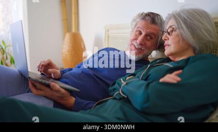 Seniorenpaar, das sich mit einem Laptop im Bett entspannt Stockfoto