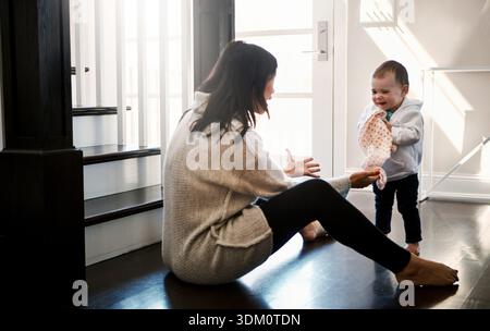 Mutter, Baby und begeistert davon, zu Hause zu gehen, um Bildung, Lernen und Bindung im Wohnzimmer zu ermöglichen. Lächeln, Entwicklung und Frauen unterrichten Kinder oder Kleinkinder Stockfoto