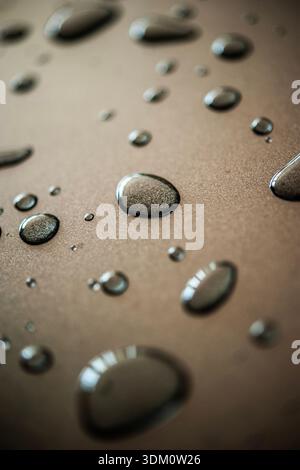 Nahaufnahme von Wassertröpfchen, die auf einer glatten Oberfläche perlen, abstrakte natürliche Textur mit Feuchtigkeit und Frische Stockfoto