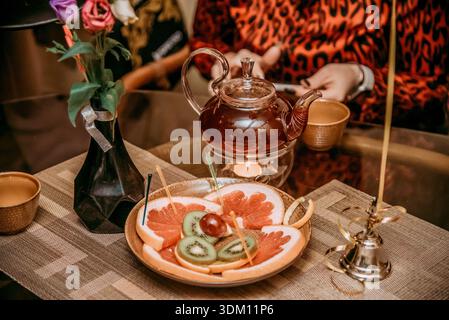 Der Kellner gießt schwarzen Tee aus der Teekanne aus Glas in einen weißen Porzellanbecher im Restaurant Stockfoto