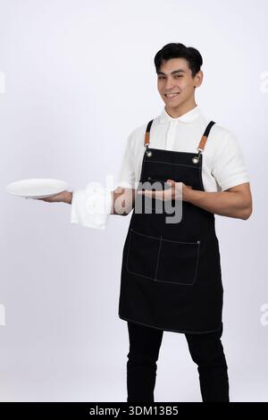Junger männlicher Kellner, der ein Tablett hält und im Studio steht Stockfoto