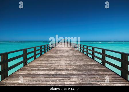 Langer hölzerner Pier im türkisfarbenen Meer vor dem blauen Himmel und dem weißen Sandstrand, Punta Cana Resort, Dominikanische Republik Stockfoto