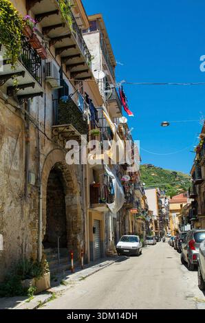Eine lange, enge Straße in Monreale, Sizilien, Italien. Wohngebäude, eine Mischung aus traditionellen Stilen und Stilen des frühen 20. Jahrhunderts, die Alterung und Abnutzung zeigen Stockfoto