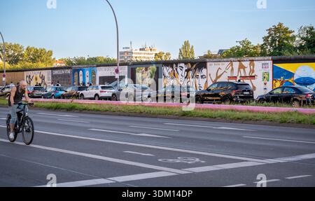Berlin, deutschland, 11. august 2023. Radfahrer auf einer Straße neben der lebhaften Ostseite Galerie, einem erhaltenen Abschnitt der berliner Mauer mit Straße Stockfoto