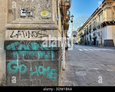 Graffiti mit der Aufschrift „Tourist go Home“ an einer Gebäudeecke entlang einer Straße in Catania, Sizilien, Italien. Stockfoto