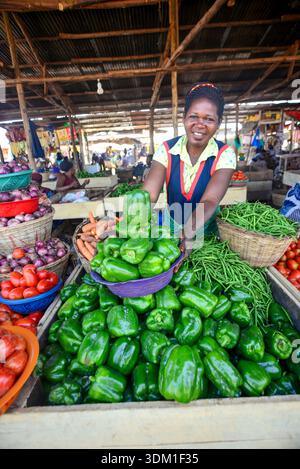 Eine fröhliche Frau verkauft frische Produkte auf dem Kalerwe Market in Kampala, Uganda, und bringt Farbe, Leben und lokalen Geschmack auf einen der geschäftigsten Märkte der Stadt. P Stockfoto