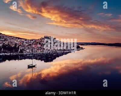 Blick aus der Vogelperspektive auf eine Küstenstadt mit Terrakottadächern, die auf das ruhige Wasser herabstürzen, das den feurigen Sonnenuntergang reflektiert, Šibenik, Kroatien. Stockfoto