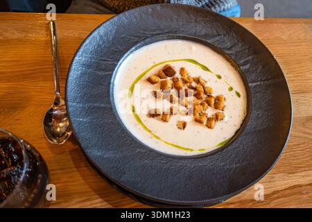 Gemischte cremige Knoblauchsuppe mit gebratenen Brotwürfeln und Öl auf schwarzem Teller auf dem Tisch, Nahaufnahme. Stockfoto