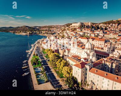 Aus der Vogelperspektive stürzen sich die Terrakotta-Dächer hinunter und treffen auf die schimmernde Adria, mit der majestätischen Kathedrale St. Jakobus, Šibenik Šiben Stockfoto