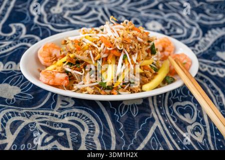 Vietnamesischer Mangosalat auf weißem Teller mit Garnelen und Essstäbchen auf ornamentalem blauweißem Hintergrund. Stockfoto