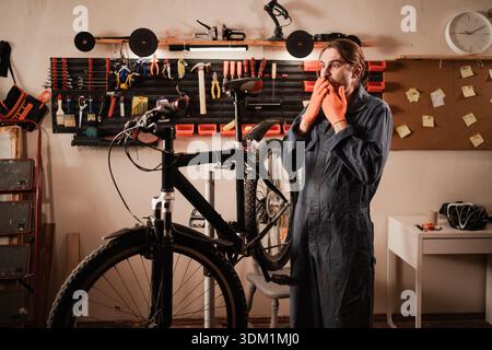 Schockiert staunte Fahrradmechaniker verdeckten den Mund während der Reparatur des Fahrrads in der Werkstatt. Beruf und Emotionskonzept Stockfoto