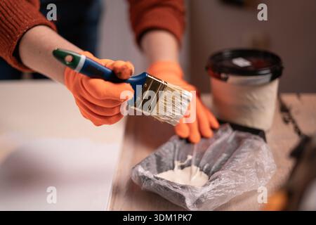 Arbeiter pflückt einen Pinsel auf einem speziellen Tablett mit weißer Farbe. Nahaufnahme von Malerhandschuhen mit Malwerkzeug Stockfoto