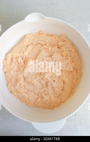 Prozess der Herstellung von selbstgemachten Linsenbrötchen. Linsen mit Vollkornmehl in einer weißen Schüssel. Gesundes veganes Backkonzept mit natürlichen Texturen und minimalem Stockfoto